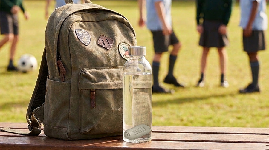 Reusable water bottle with GOpure Pod beside a school backpack on a sports field