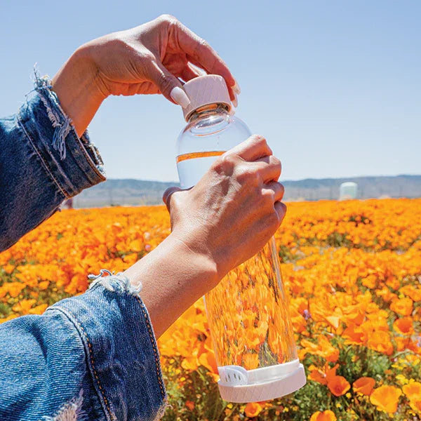 Reusable water bottle with GOpure purifier in flower field for clean water on the go.